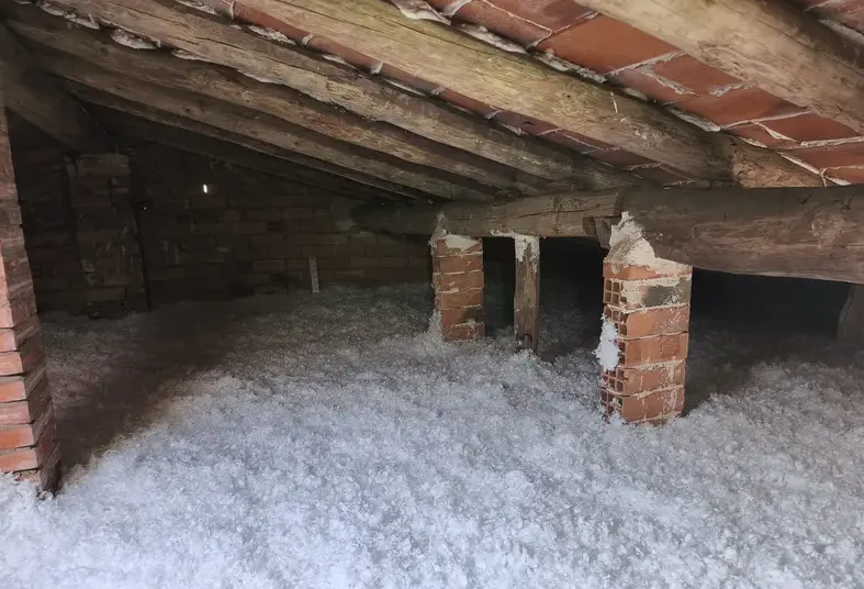 Desván de ladrillo con vigas de madera y el material extendido por todo el suelo